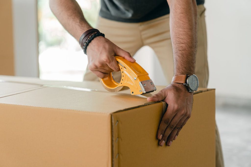 Crop man taping carrying box with scotch
