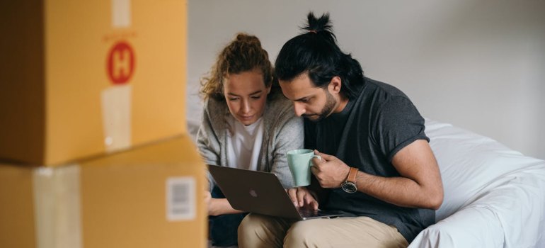 Young multiethnic couple watching laptop while moving house