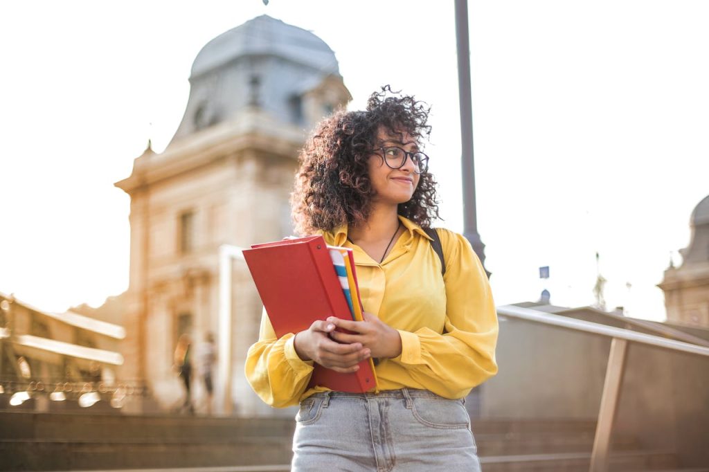 Woman In Yellow Jacket Holding Books and thinking about student movers Boston offers