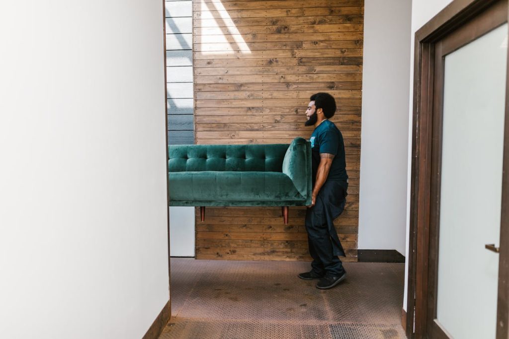 Man in Blue Denim Jeans carrying Green Sofa
