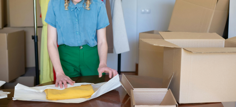 Person packing clothes in cardboard boxes using sustainable materials, representing green moving tips to lower your carbon footprint.